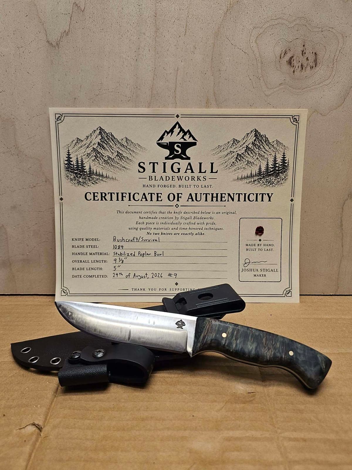 Bushcraft knife with a dark stabilized poplar burl handle and a Kydex sheath with belt clip, in front of its signed certificate of authenticity